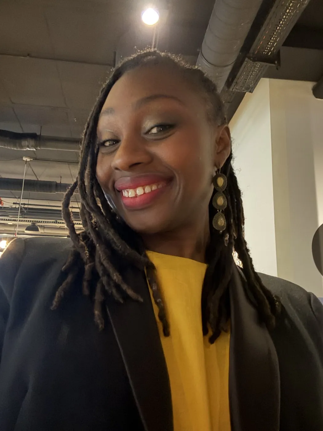 Fatoumata souriante, top jaune et blazer noir, en sortie